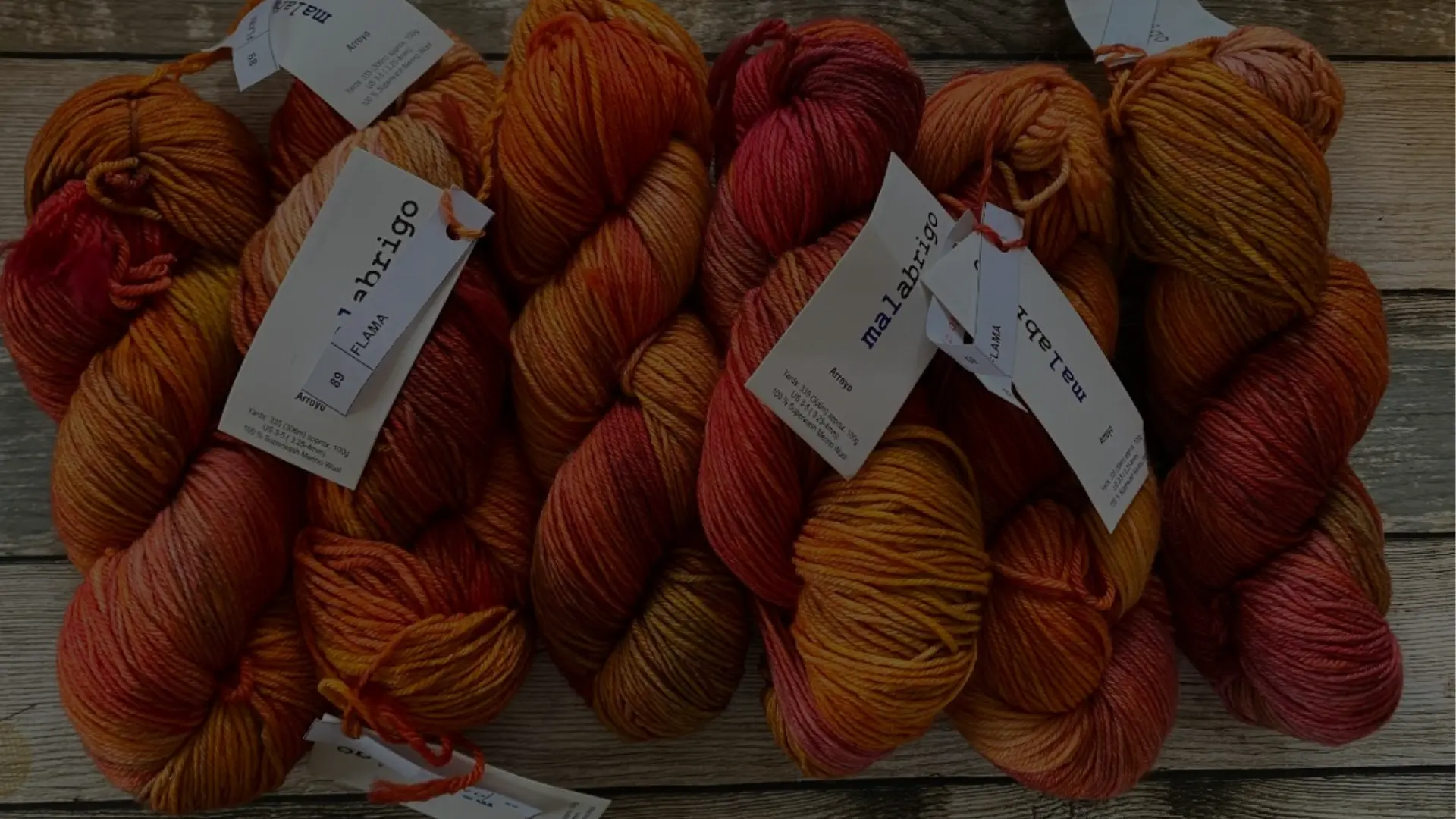 Garn i varma nyanser – Teija - Textil i Järfälla Närbild på garnhärvor i orangea och röda toner på träbord – Teija - Textil i Järfälla