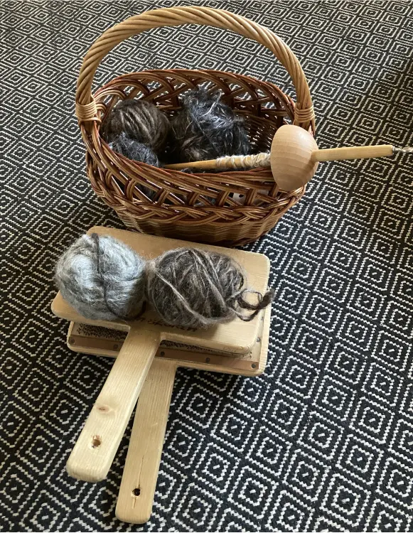 Slända och kardor – Teijas kärlek till gamla hantverkstekniker Korg med garn och slända på ett mönstrat tyg – traditionellt textilhantverk i fokus